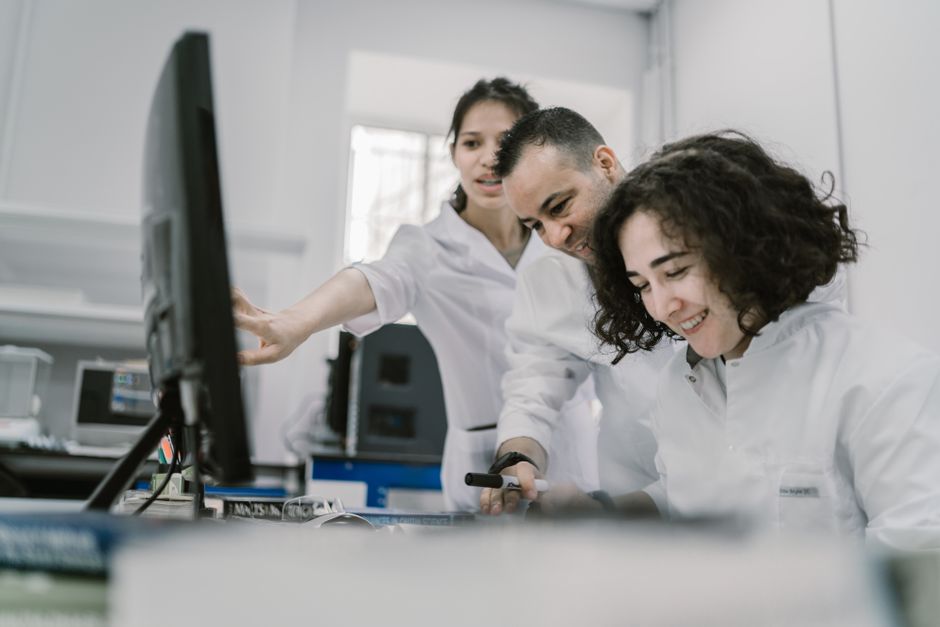 Group of diverse scientists working together on a computer in a bright, modern laboratory.