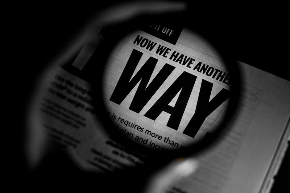 Black and white close-up of newspaper text magnified through a lens, emphasizing the word 'WAY'.